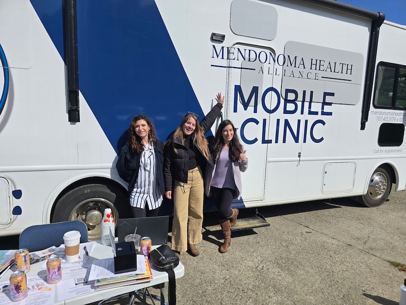 3 women stand in front of the Mendonoma Health Alliance Mobile Health Bus